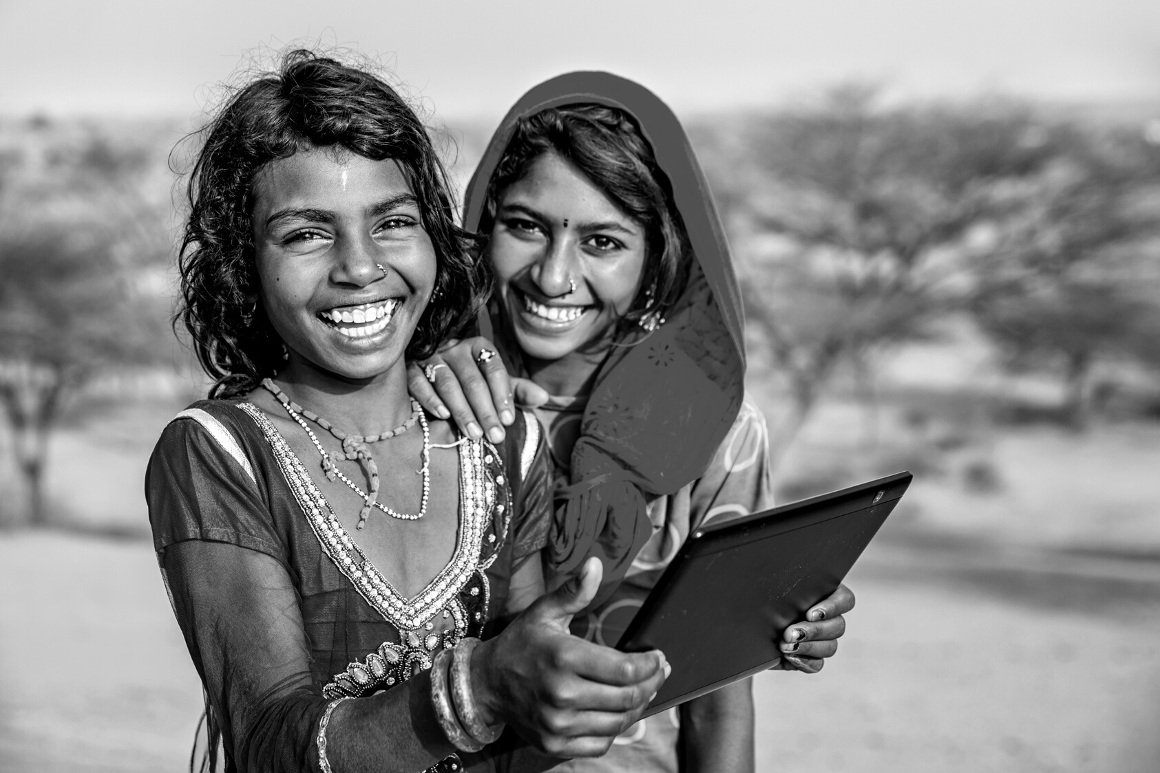 Happy Indian young girls using digital tablet, desert village, India